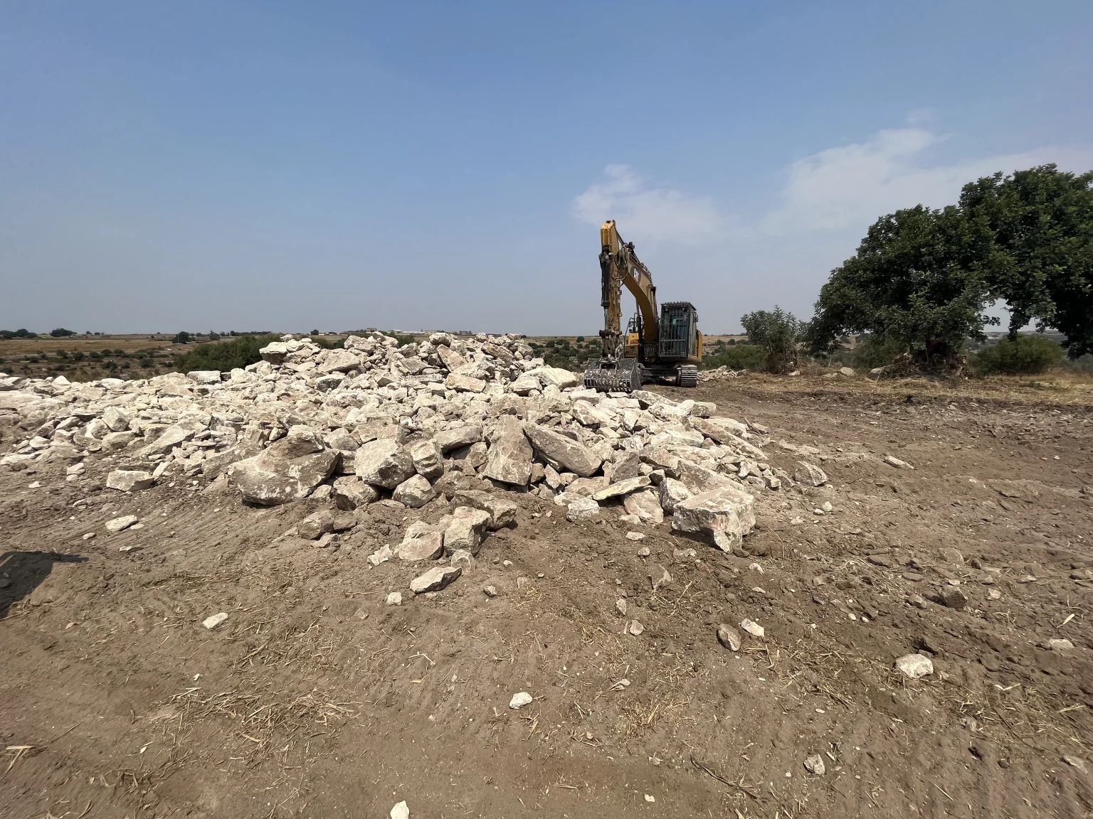 Spietramento di un fondo agricolo: cumulo di pietre ed escavatore